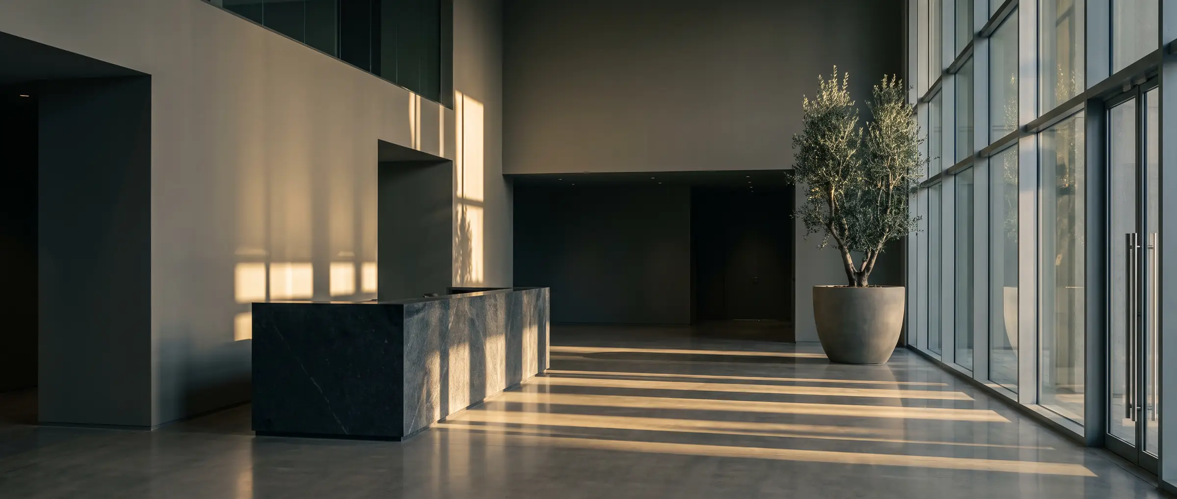 Empty double-height commercial lobby in late afternoon light with long shadows across polished concrete