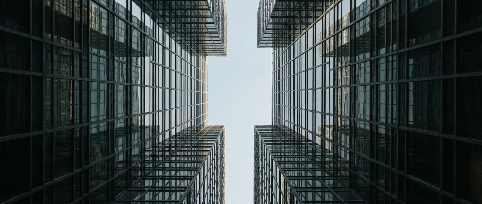 Upward view between two modern financial district office towers converging toward a strip of sky