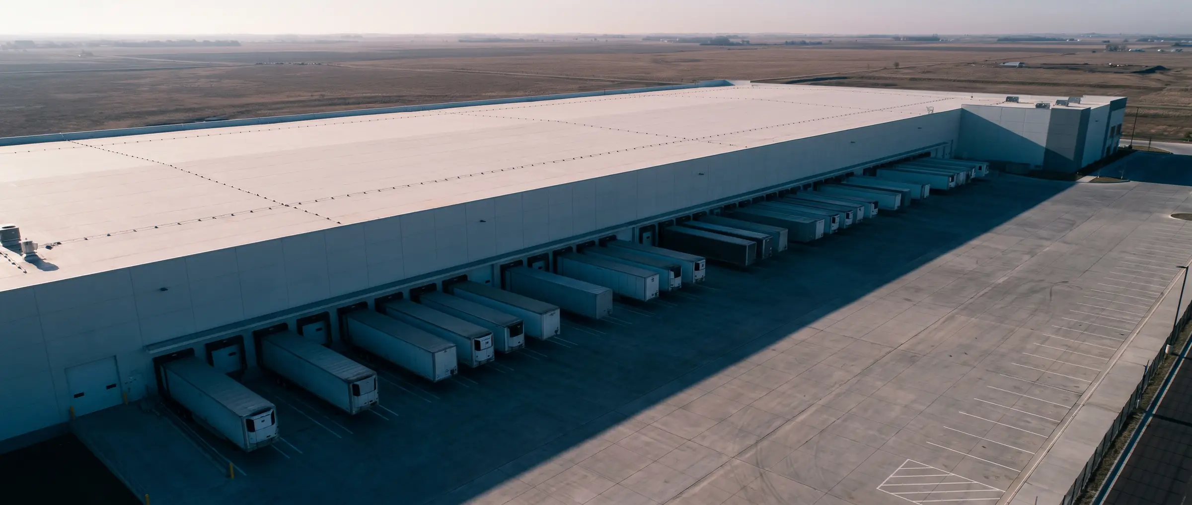 Aerial view of a modern distribution warehouse with loading docks, trailers, and a wide truck court