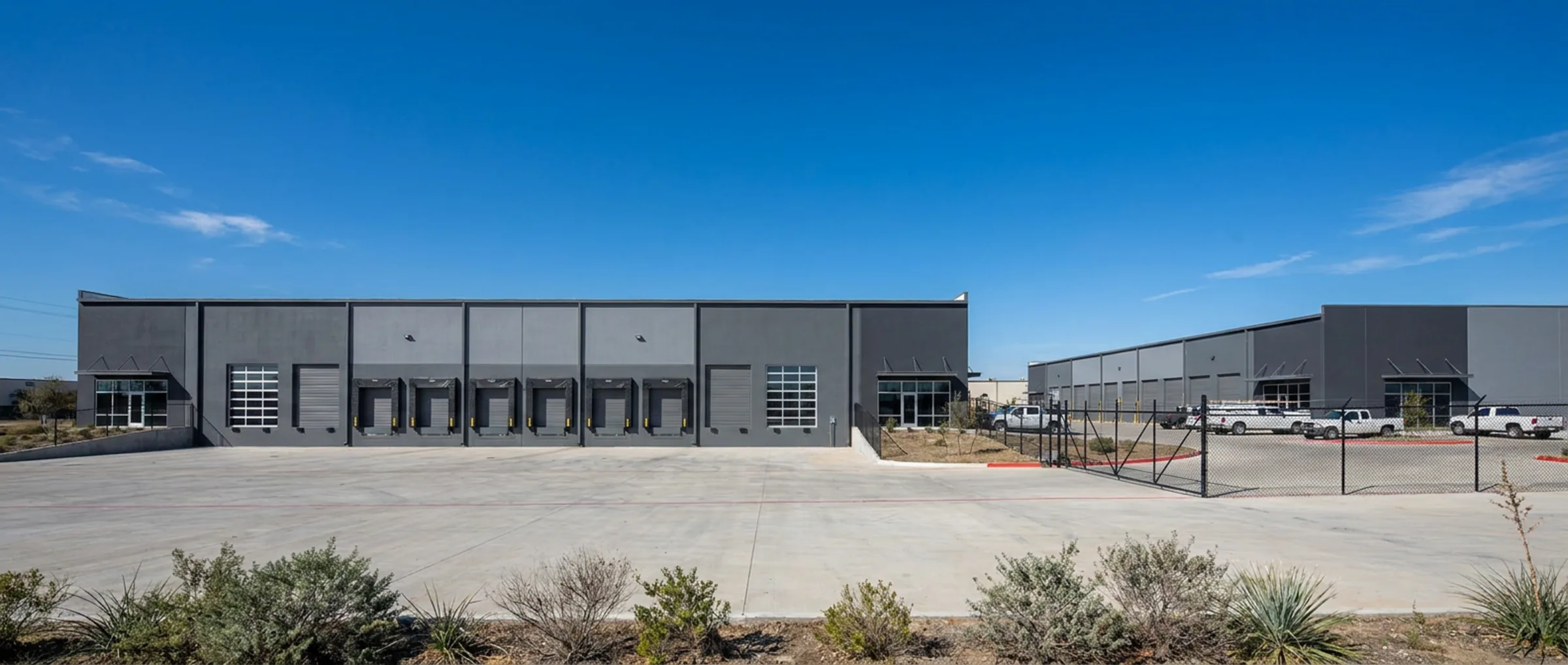 Two modern small-bay industrial buildings with dock and grade loading behind a fenced concrete yard