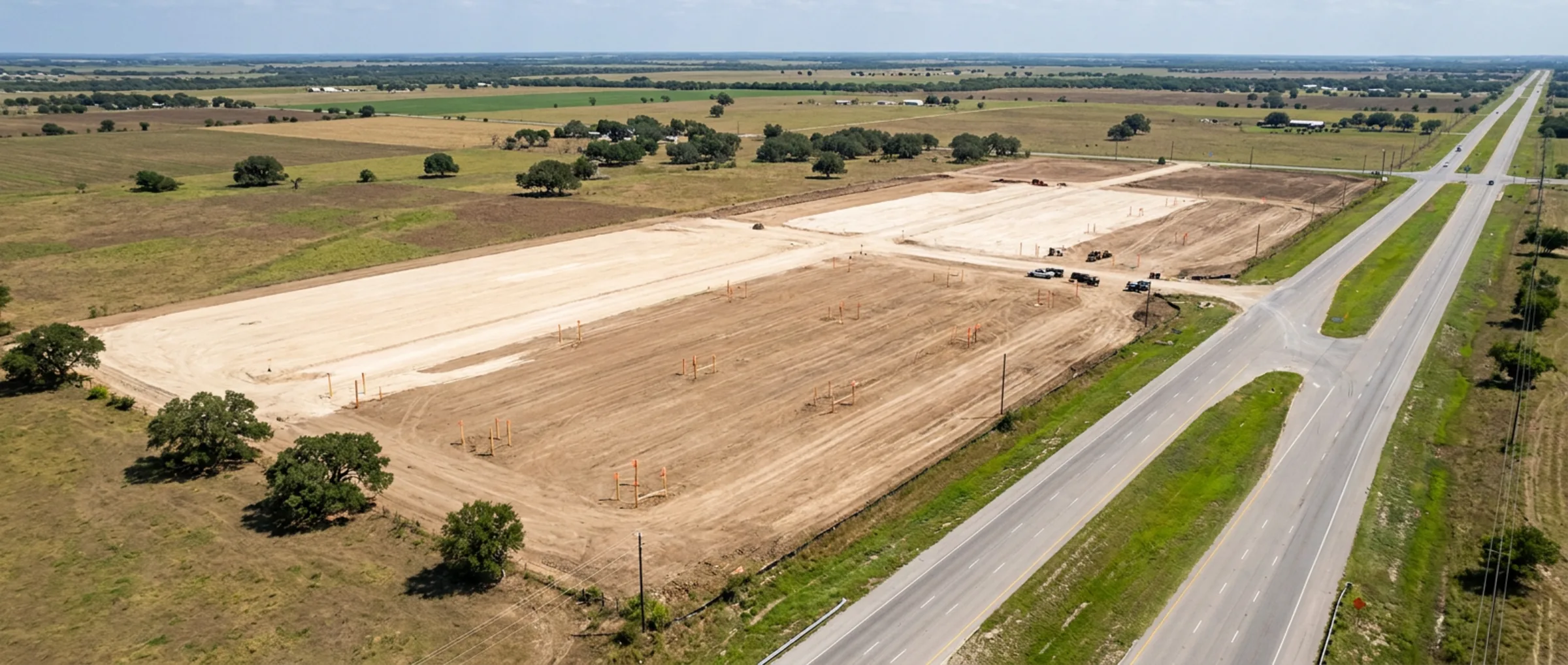 Aerial view of a large cleared and graded development tract beside a highway, with open Texas farmland beyond