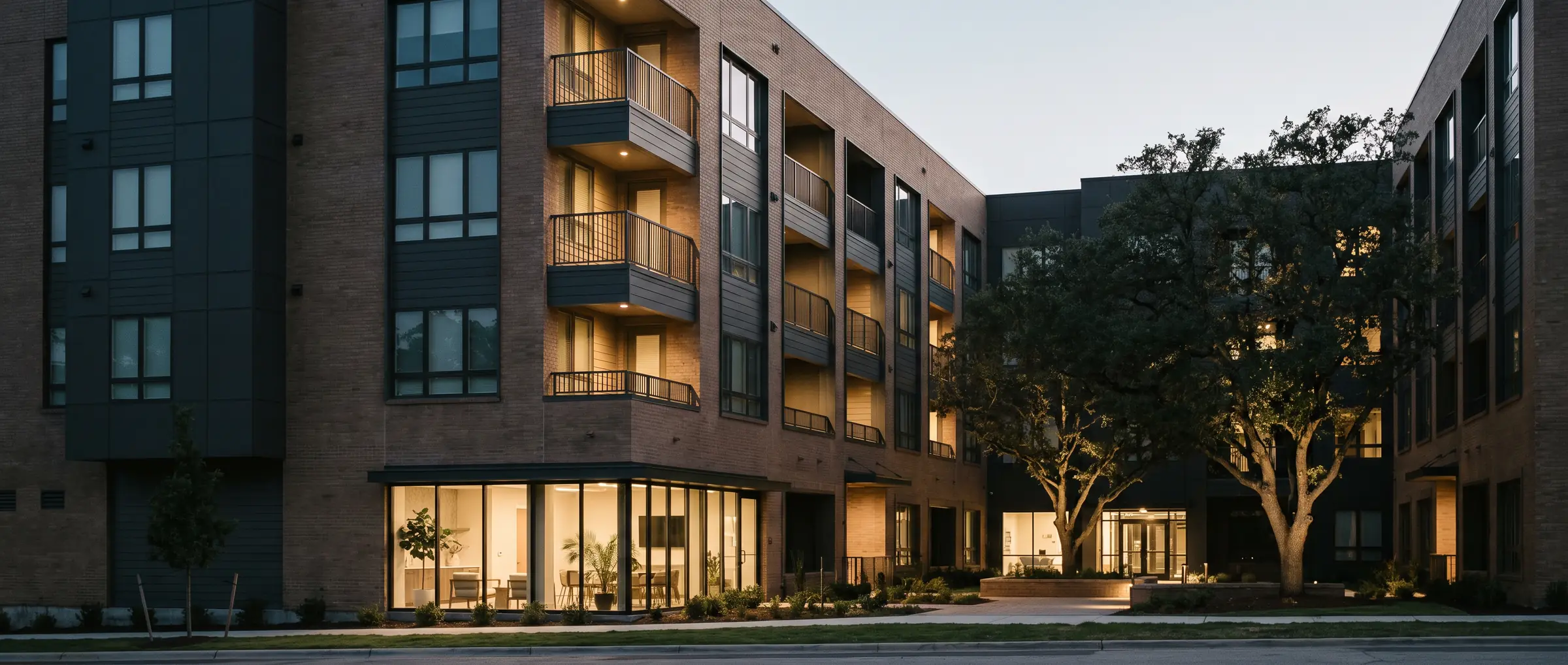 Newly completed five-storey multifamily building at dusk with articulated brick facade and rhythmic balconies