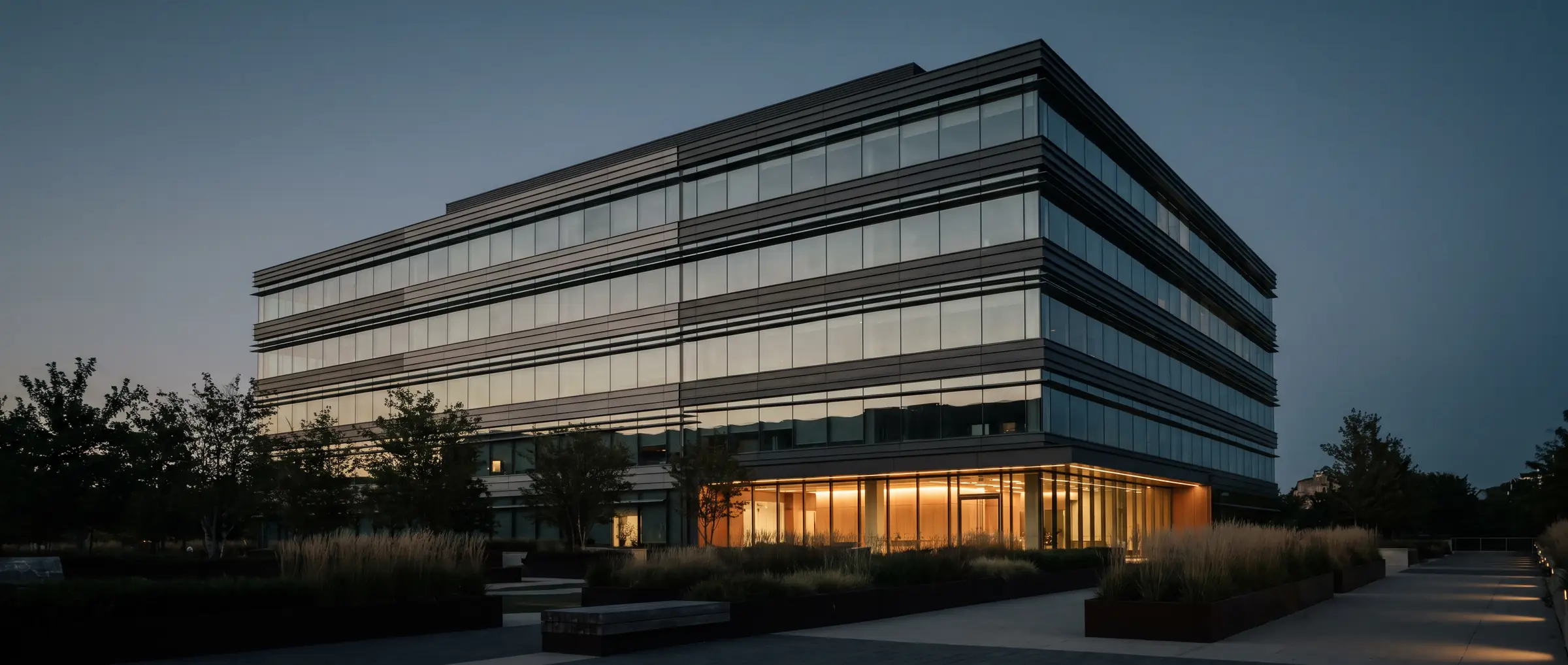 Modern mid-rise office building at dusk with horizontal glazing bands and a lit ground-floor lobby