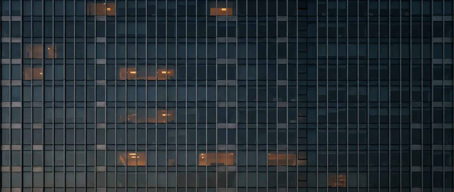 Abstract grid of a glass office tower facade at dusk with a scattered pattern of lit window bays