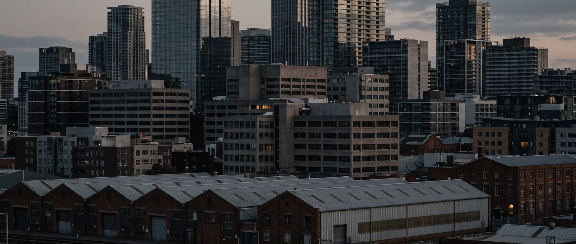 Telephoto view of a mixed commercial district at dusk with warehouses, mid-rise blocks, and towers layered together